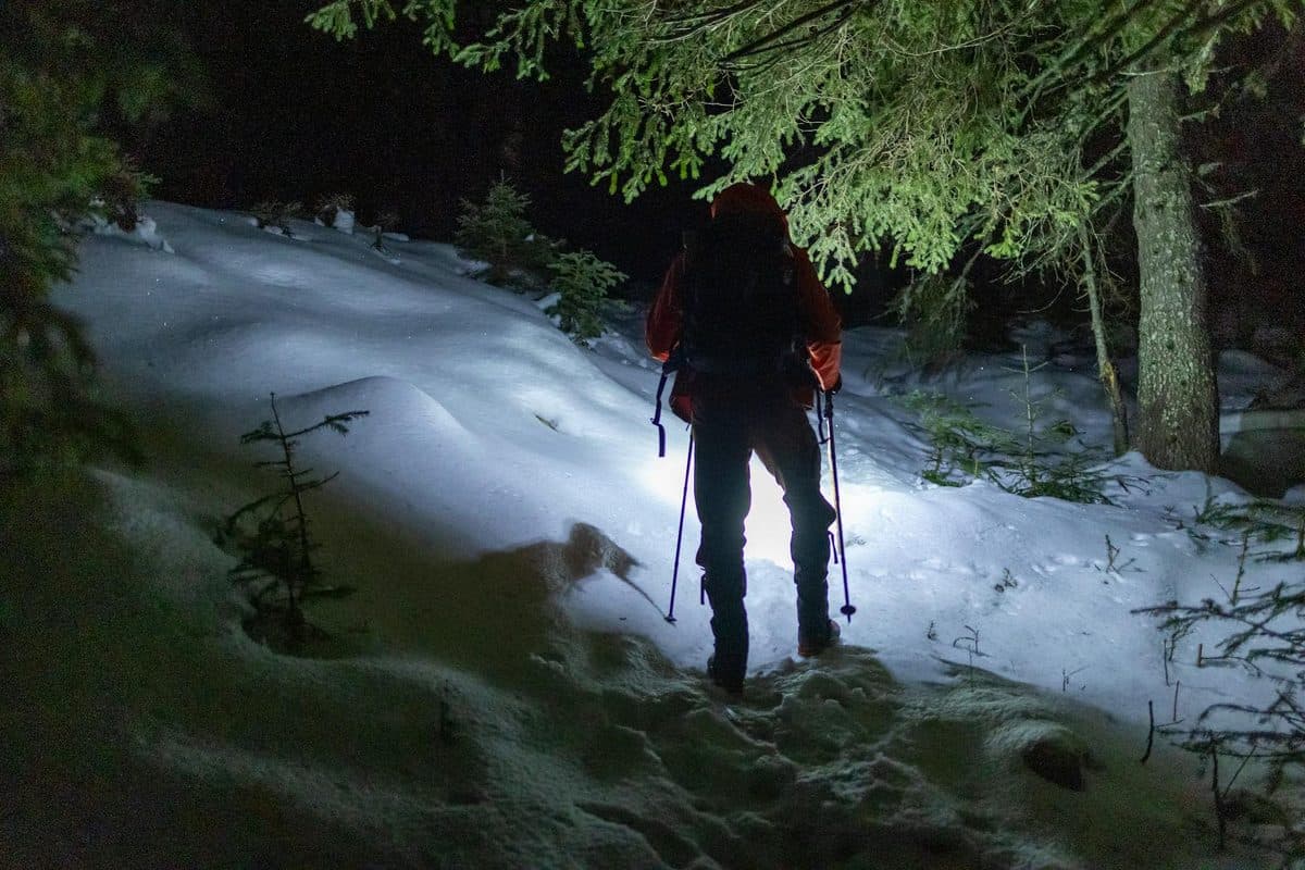 Hiker venturing through a snowy forest at night